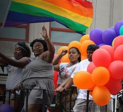 Pride Parade participants along with balloons and rainbows on a float