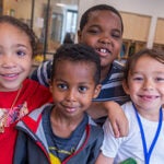 Four young students smile for a photo in a classroom.