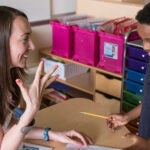 A teacher talks with a young student in a classroom