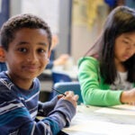 A young student sits in a classroom and poses for a photo