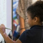 Young student works at a math problem at a white board in a classroom