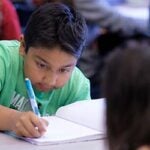 An elementary student writes in a notebook in a classroom