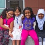 Four students sit together on a playground and smile for a photo