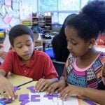 Two students work together at a desk in a clasroom