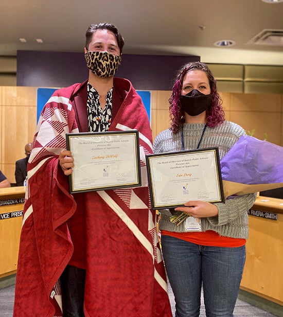 Directors DeWolf and Dury stand together holding certificates in the auditorium