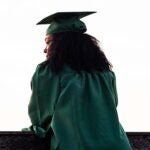 A graduate in a cap and gown looks out over a balcony