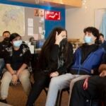 A teacher and students in masks talk in a classroom