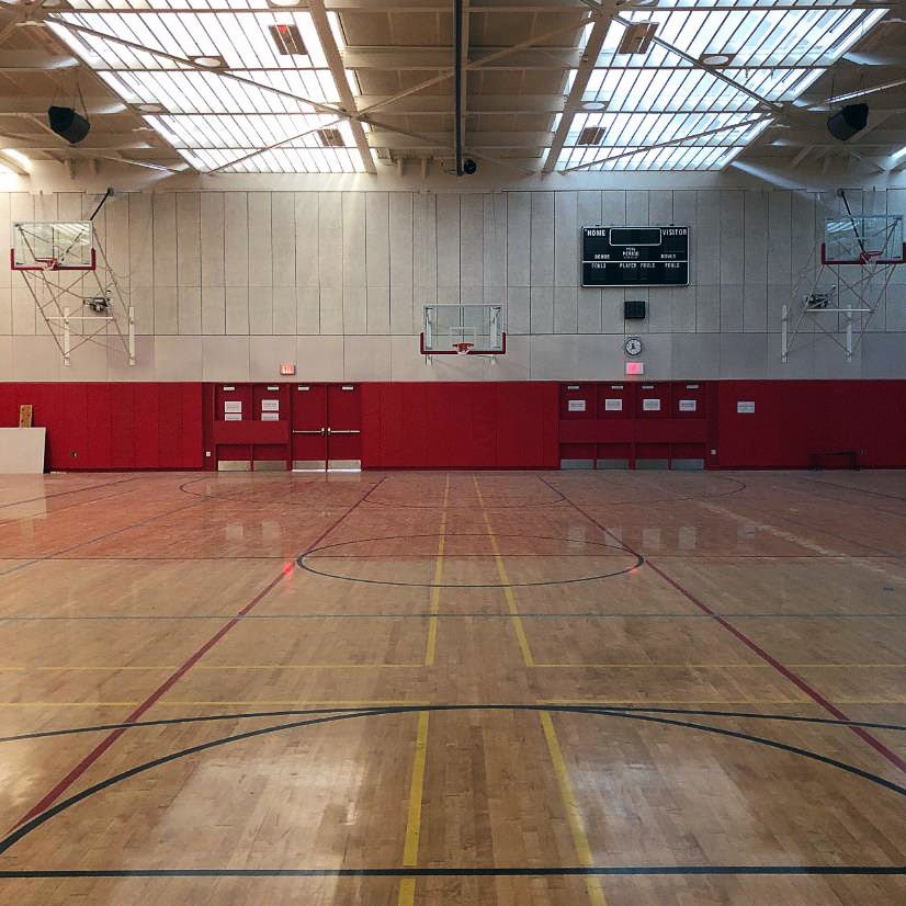 partial view of a gymnasium with a wood floor, protective padding on lower part of wall, and skylights