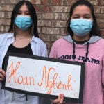 Two students in masks hold a sign that says welcome in vietnamese