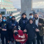 A group of students and adults pose for a photo on top of a building in downtown Seattle.