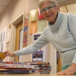 A school library volunteer stands at a table with several elementary age books