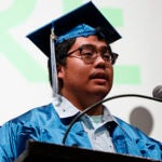 A graduate in cap and gown stands at a podium during a graduation ceremony