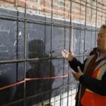 A man in construction vest stands before a blackboard