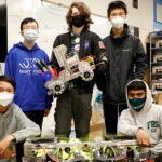 A group of five student pose for a photo with a robotics project in a classroom.