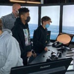 Three students and an adult stand on a boat deck.