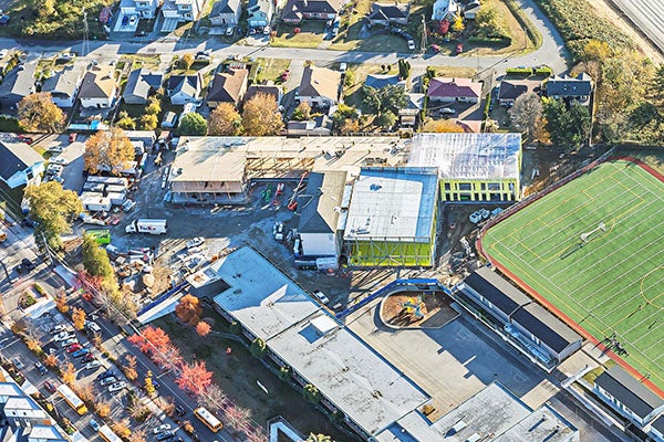 aerial view of a construction project that wraps around an existing building with a playfield to the right