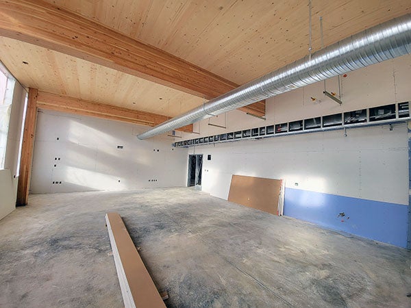 a large room with wood beams and a wood celing has unfinished walls and floor with a metal duct near the ceiling