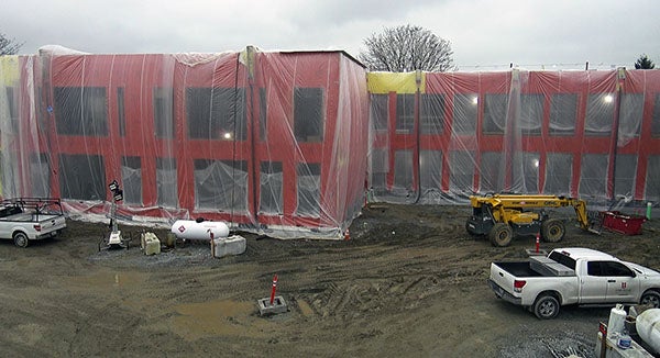 a 2-story building under construction with plastic draped over it - the walls are orange, there are empty spaces for windows, and there is dirt and construction equipment in front