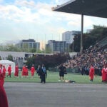 Two groups of graduates in cap and gown line up at Memorial Stadium
