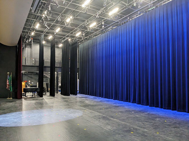 a stage with lighting in the ceiling has blue curtains