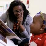 An educator and a young student talk together in a classroom while looking at a book.