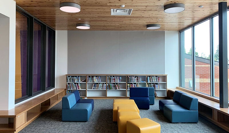 a group of low soft seating in a nook between two windows with a low bookshelf on the back wall