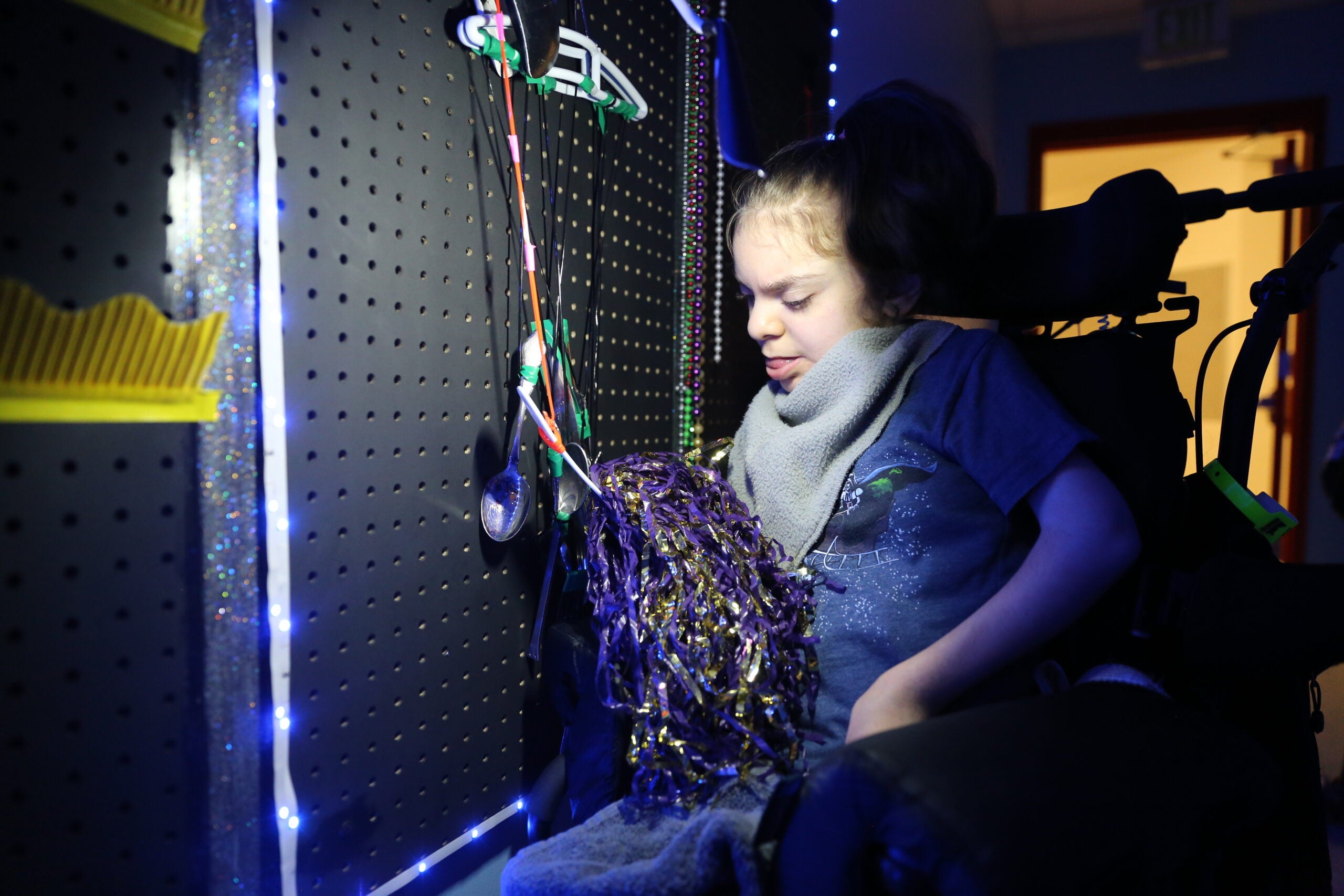 Student plays with purple and gold pom pom on sensory wall.
