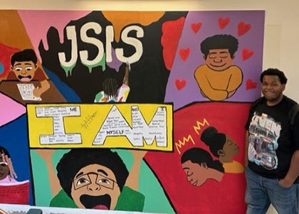 A young man poses by the mural he painted in a school
