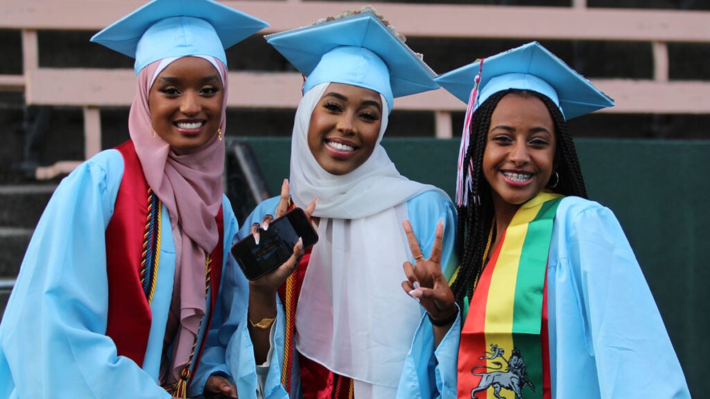 Three graduates smile for a photo in cap and gown