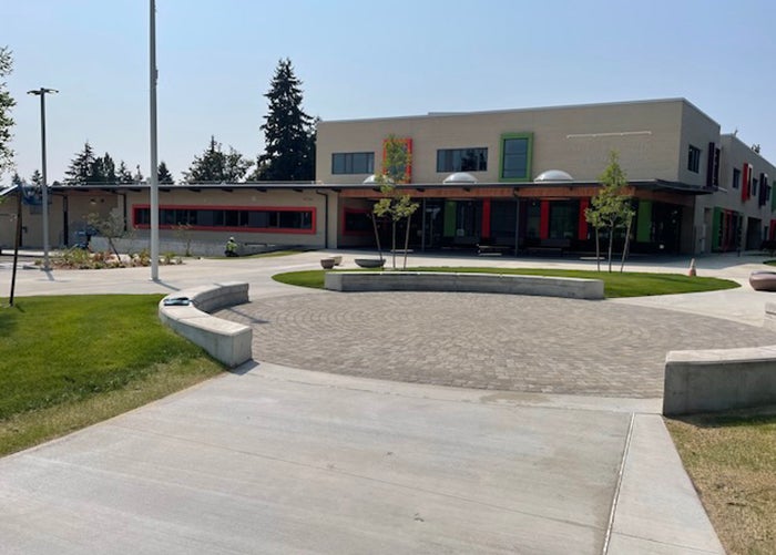 a white brick building has a one story section to the left and a two story section to the right. the building has orange trim. a circular plaza is in front surrounded by grass