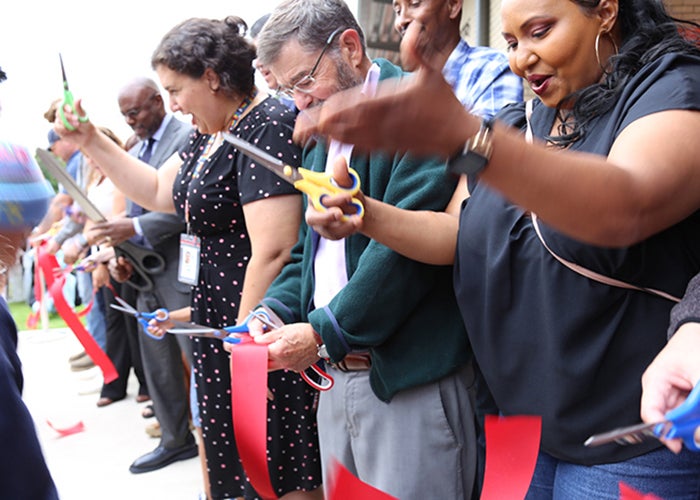 A group of people face one direction with scissors in their hands and pieces of red ribbon