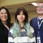 Three people smile for a photo in a school classroom.