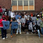 a group of young men stand in front of a brick building holding up shirts