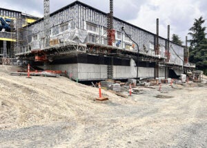 exterior of a partially construction building with large concrete blocks below and a scaffold walkway where bricks are being installed on the walls