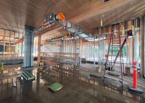Interior of the building showing metal wall frames, ductwork, and a wet floor reflecting the construction overhead.