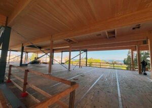 Open upper floor with wooden surfaces and large windows offering a scenic view of trees and sky.