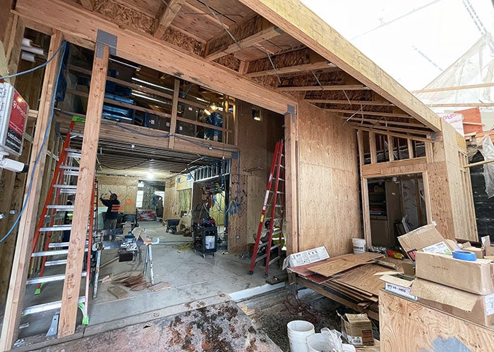 Entry view of a building under construction, with exposed wood framing, wiring, and construction materials scattered throughout.