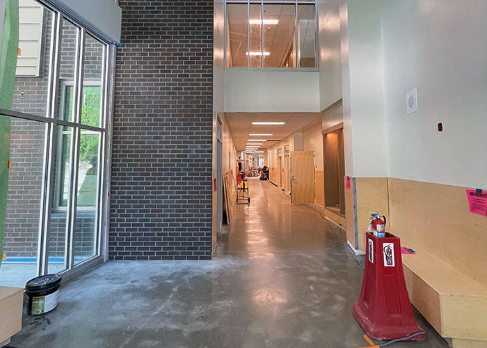 A clean, modern hallway inside the school with polished concrete floors, light-colored walls, and large windows along one side.