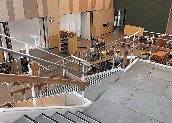 View from the top of a staircase overlooking a commons area with supplies and construction tools scattered throughout.