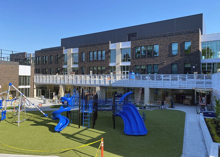 View of a colorful playground set in front of the modern school wing, with large windows and a wraparound outdoor walkway.