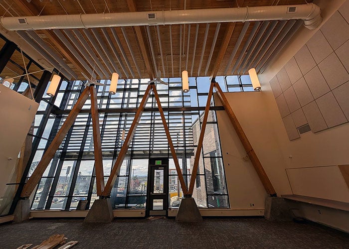 A tall interior space with angled wooden beam supports and large glass windows, allowing natural light to fill the room.
