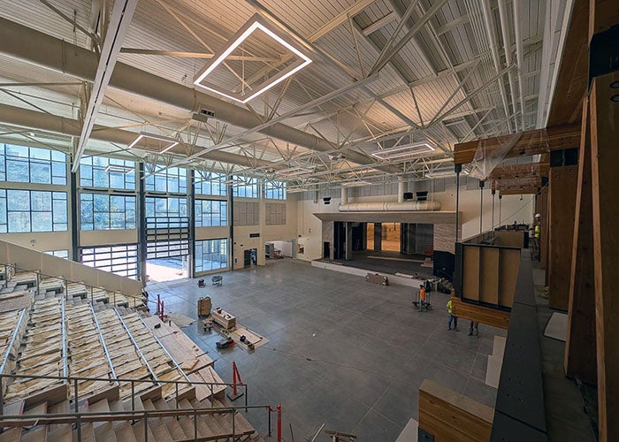 A wide open performance space featuring a large stage, high ceiling with modern lighting, and tiered seating under construction.
