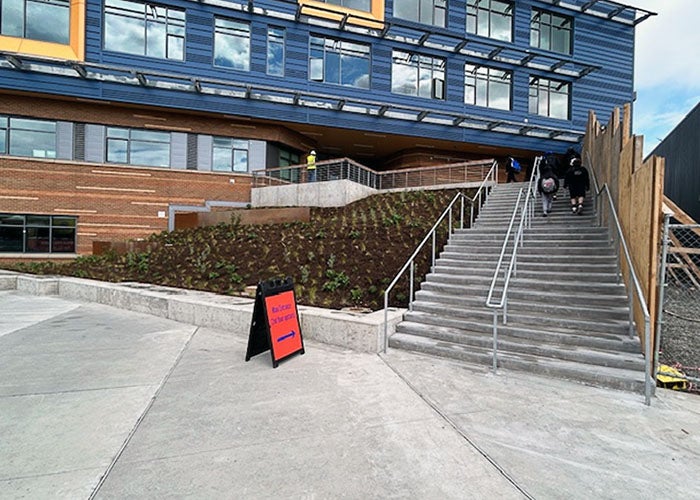 Exterior staircase next to a newly planted slope leading up to the main school building, with a blue and orange color scheme.