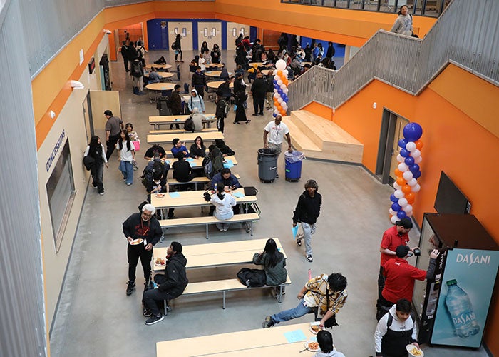 Students and staff gather in the commons for a welcome event, with orange walls, benches, and balloon decorations.