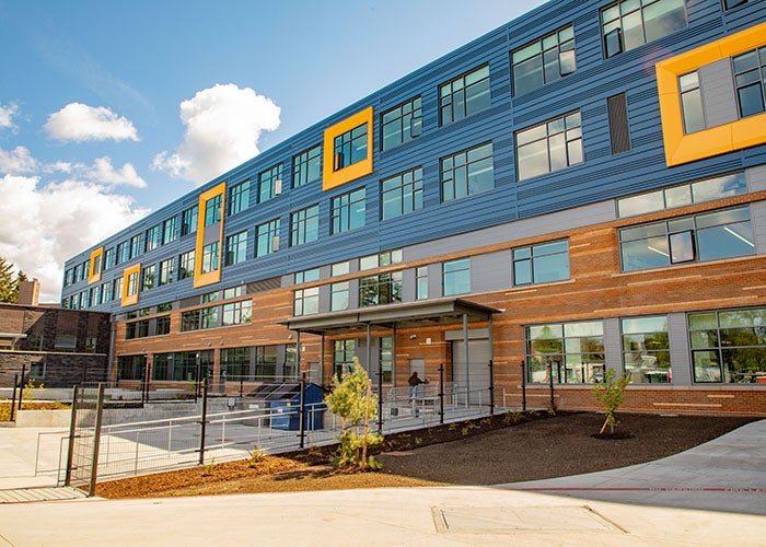 Exterior view of the school’s north side with brick, metal paneling, and yellow window accents under a blue sky.