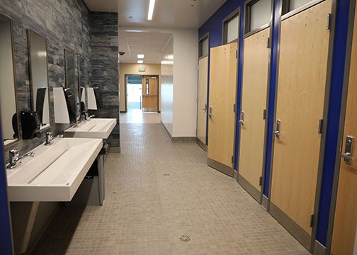 Restroom corridor with private single-occupant stalls on one side and modern shared sink fixtures on the other.