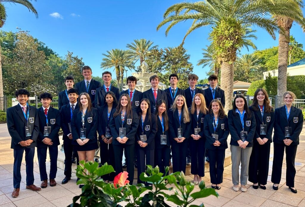 Students wearing suits pose in front of palm trees