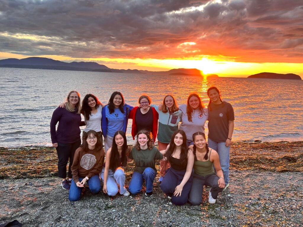 Group of students standing in front of large body of water and sunset