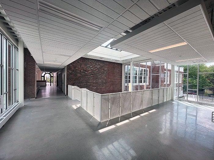 A bright hallway on the upper floor with polished concrete floors and large windows overlooking the surrounding neighborhood. The corridor features modern lighting and transitions between the original brick building and newer construction.