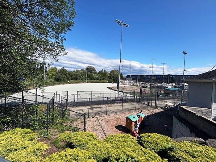 A fenced-in outdoor sports field with stadium lighting poles, surrounded by a black chain-link fence.